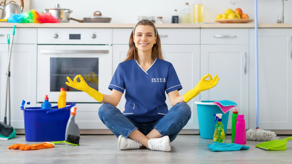 Domestic worker in uniform sitting with cleaning tools ready for home service in Ajman